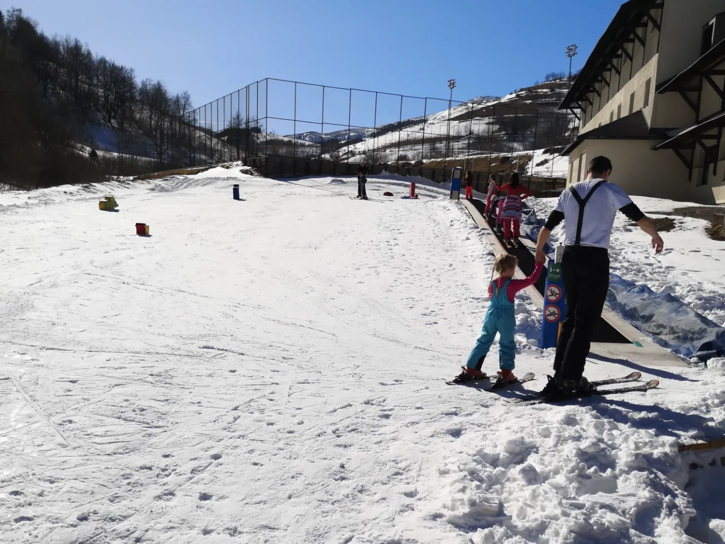 The learning slope at Hotel Junior: a little girl on skis holds an adult’s hand next to the magic carpet